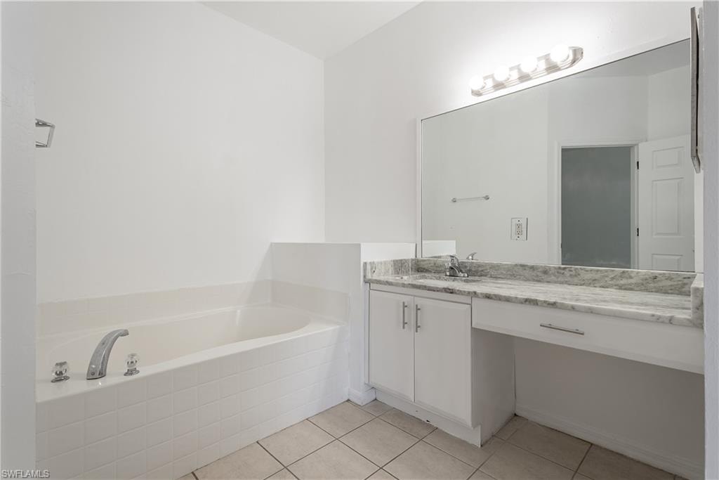 Bathroom featuring a built-in soaking tub with white tile surround, a vanity with white cabinetry, a single basin sink, a stone-finish countertop, and a large wall-mounted mirror with overhead lighting