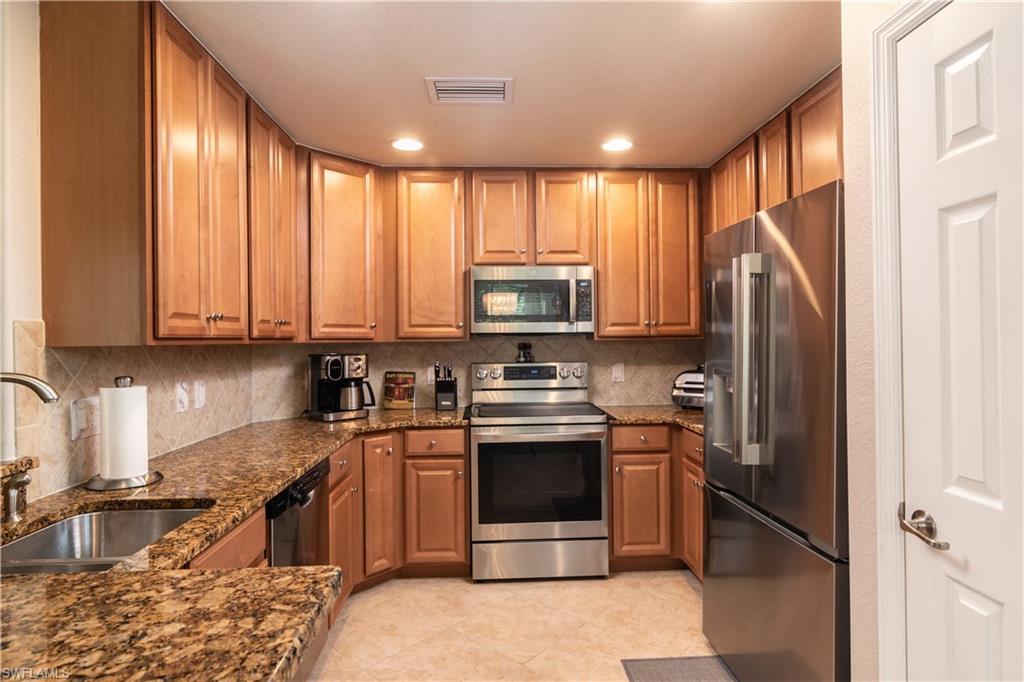 U-shaped kitchen featuring wood cabinetry, granite countertops, stainless steel appliances, and a tiled backsplash