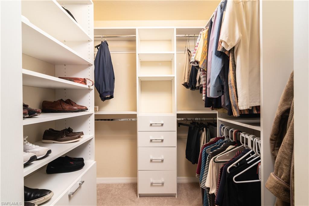 Custom closet system featuring multiple hanging rods, adjustable shelving, integrated drawers with silver hardware, and carpeting