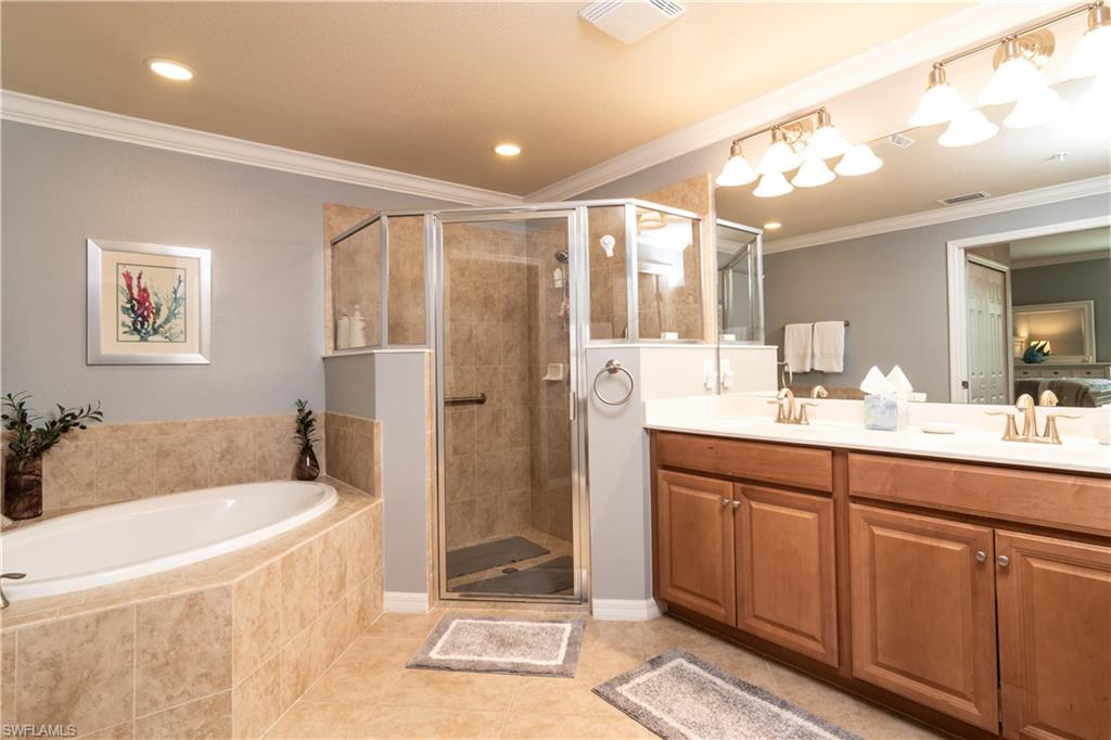 Spacious bathroom featuring a dual vanity with wood cabinetry, a tiled soaking tub, and a separate glass-enclosed shower