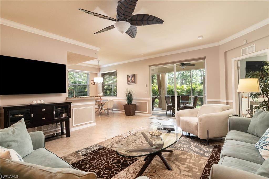 Spacious living area featuring tile flooring, crown molding, a ceiling fan, and sliding glass doors leading to a screened lanai