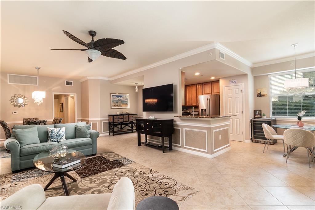Open-concept living space featuring neutral tile flooring, crown molding, and a built-in kitchen pass-through with a granite-style countertop