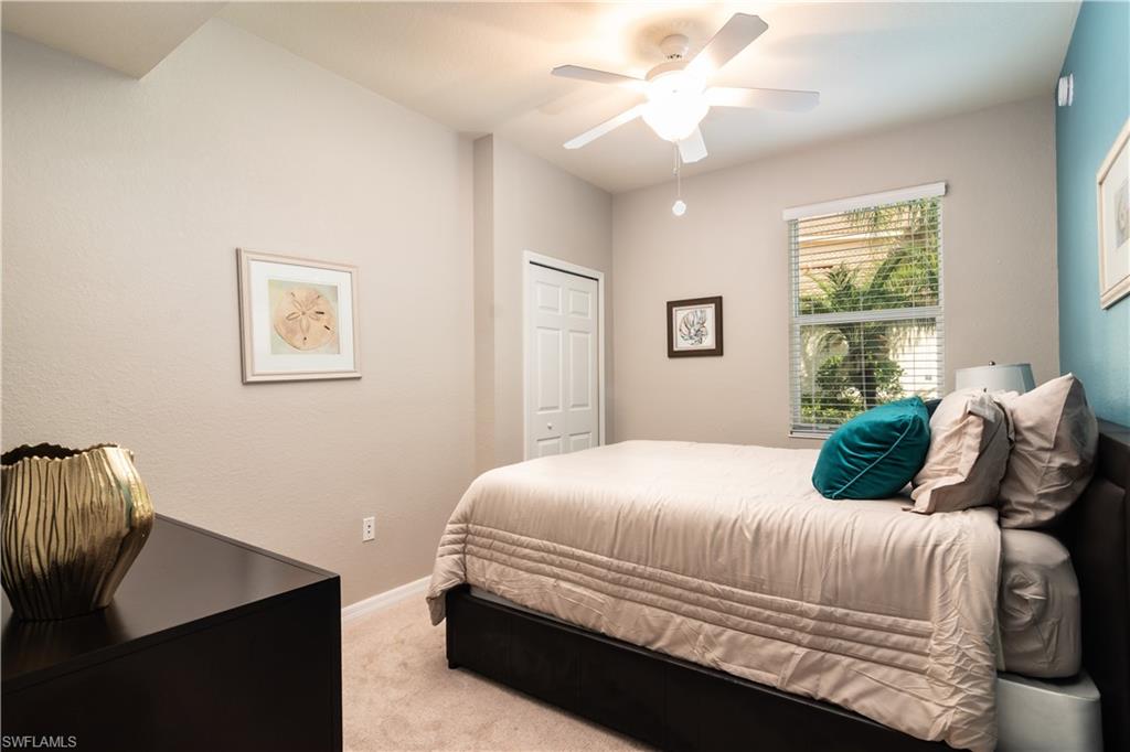 Carpeted guest bedroom featuring a ceiling fan with integrated lighting, a window with horizontal blinds, and a built-in closet with a bi-fold door