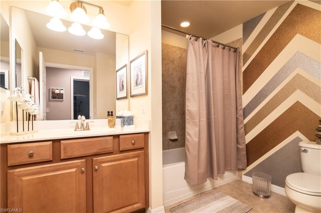 Full guest bathroom featuring a single vanity with wood cabinetry, a large mirror, and a shower-tub combination with a tiled surround