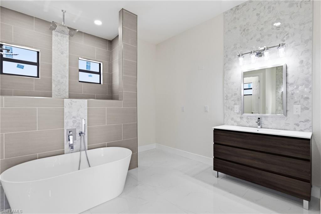 Full bathroom with vanity, tile walls, a freestanding bath, light marble finish flooring, and recessed lighting