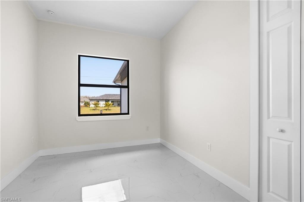 Unfurnished room featuring light marble finish flooring and baseboards