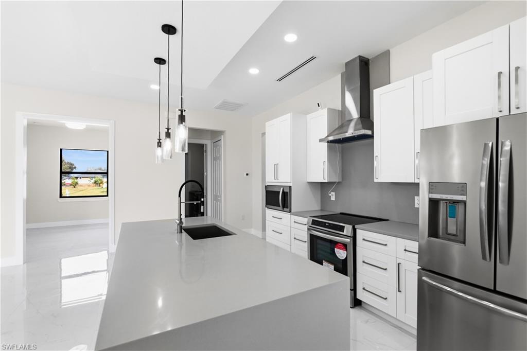 Kitchen with stainless steel appliances, white cabinets, pendant lighting, an island with sink, and light marble finish flooring