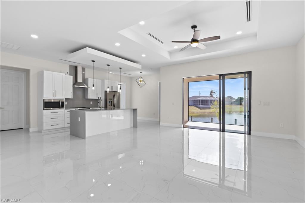 Kitchen featuring white cabinets, an island with sink, pendant lighting, open floor plan, and a tray ceiling