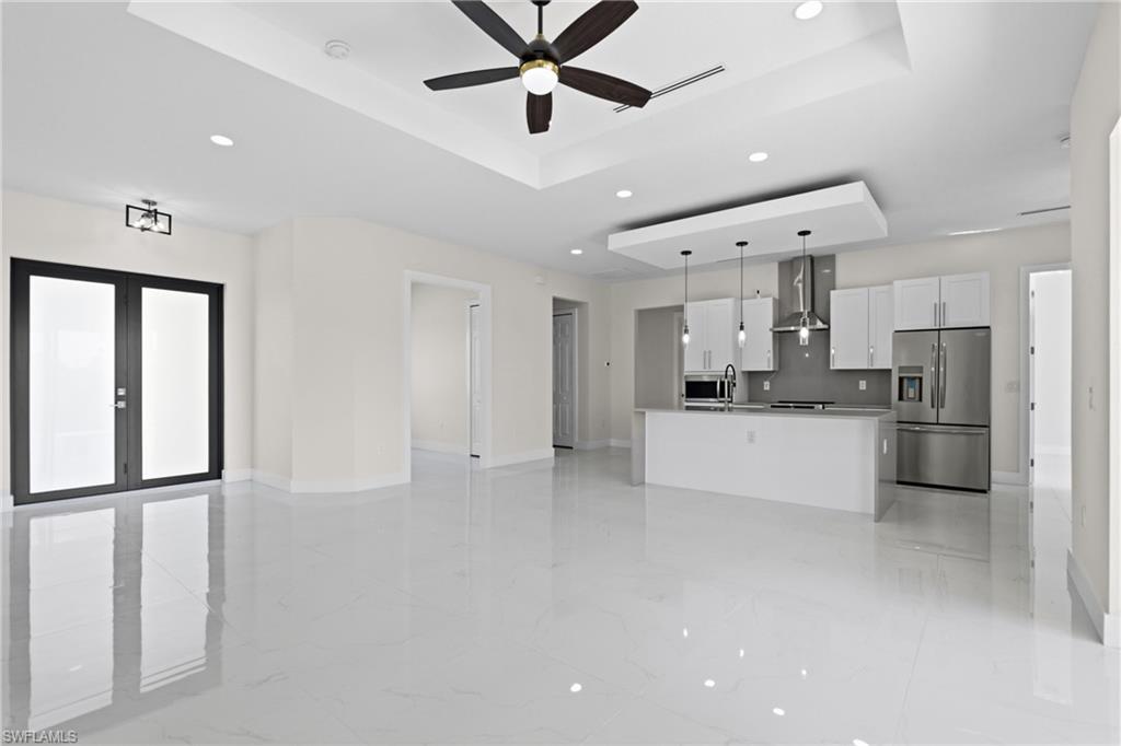 Kitchen with open floor plan, a raised ceiling, white cabinets, light marble finish flooring, and stainless steel refrigerator with ice dispenser