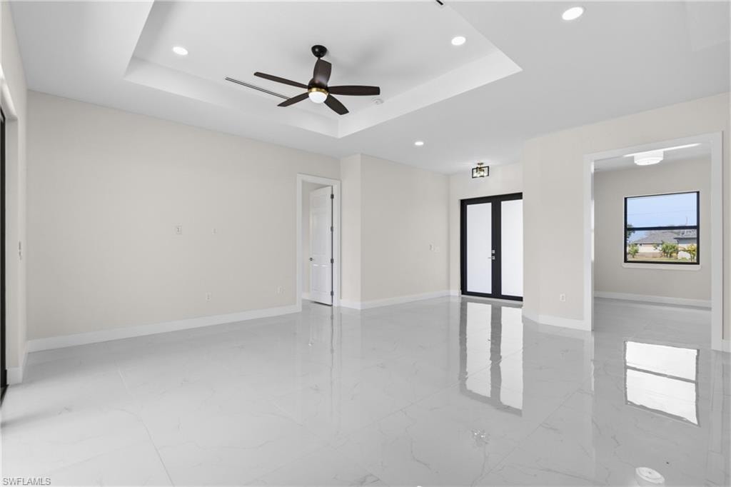 Spare room featuring recessed lighting, french doors, ceiling fan, light marble finish flooring, and a tray ceiling