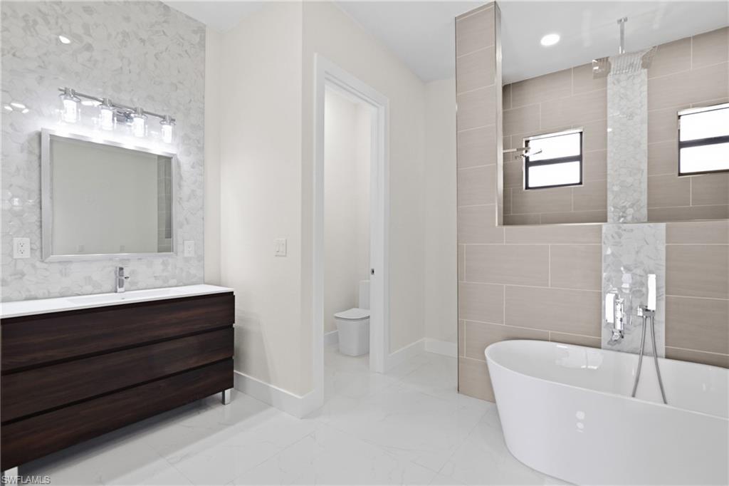 Full bath with tile walls, vanity, a freestanding bath, light marble finish floors, and tiled shower