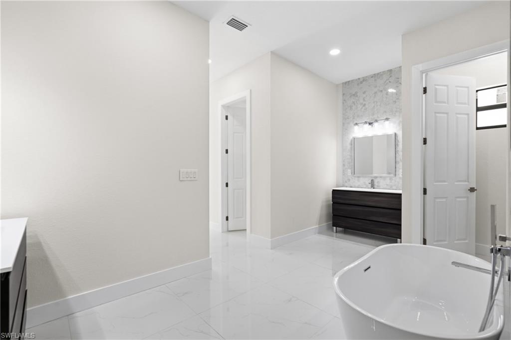Bathroom featuring vanity, a freestanding tub, light marble finish flooring, and recessed lighting