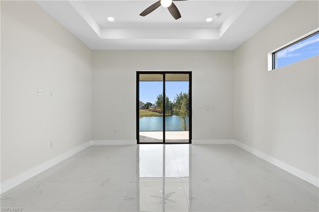 Spare room with light marble finish floors, a tray ceiling, ceiling fan, a water view, and recessed lighting