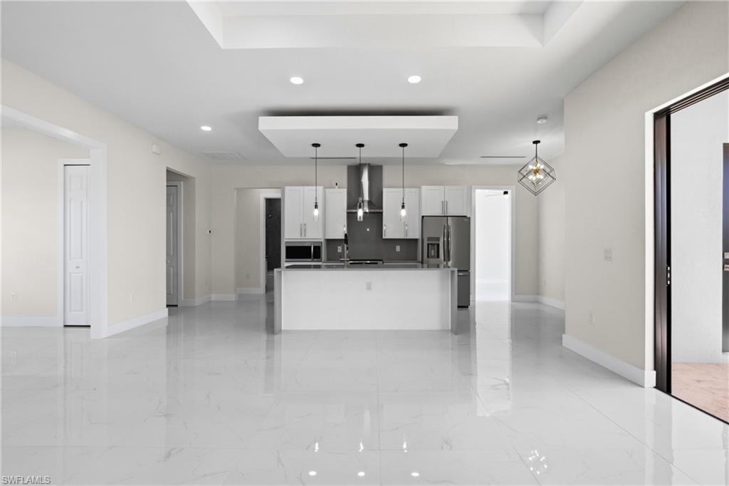 Kitchen with white cabinets, open floor plan, stainless steel fridge with ice dispenser, a kitchen island with sink, and light marble finish floors