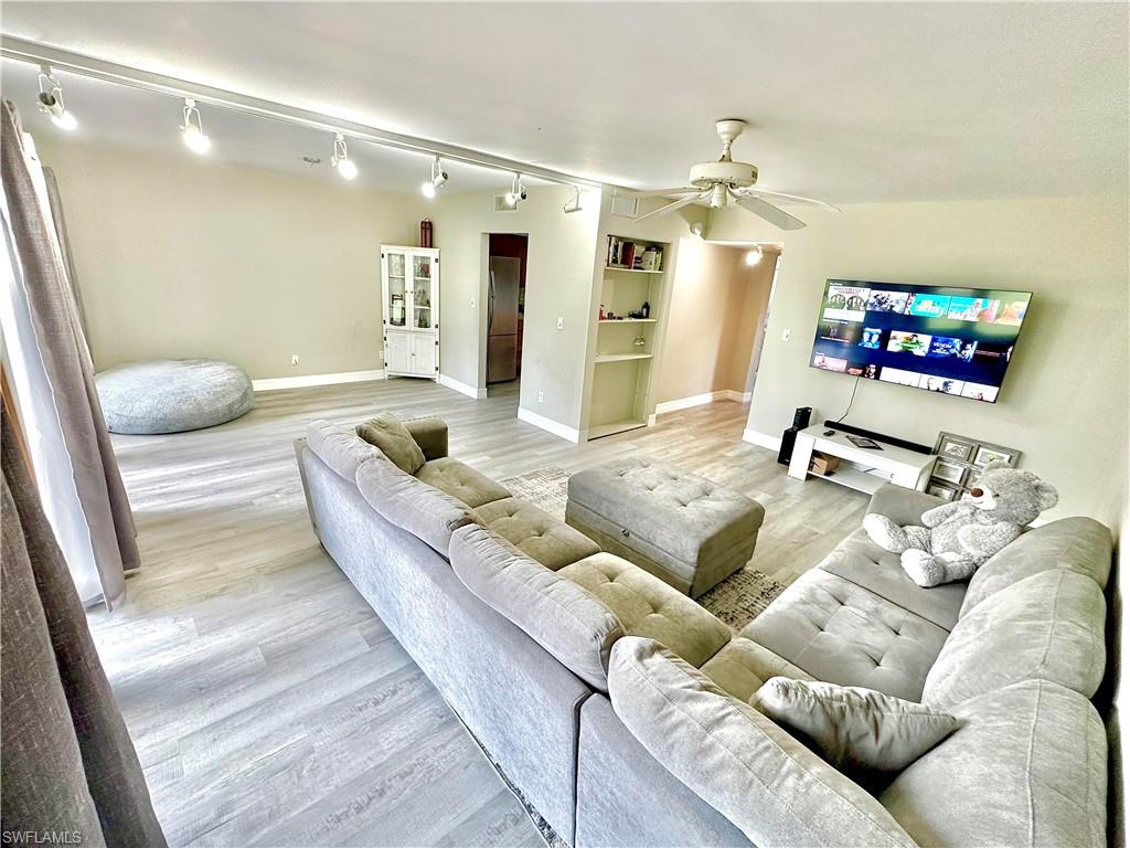 Spacious living area featuring wood-finish flooring, track lighting, and a ceiling fan