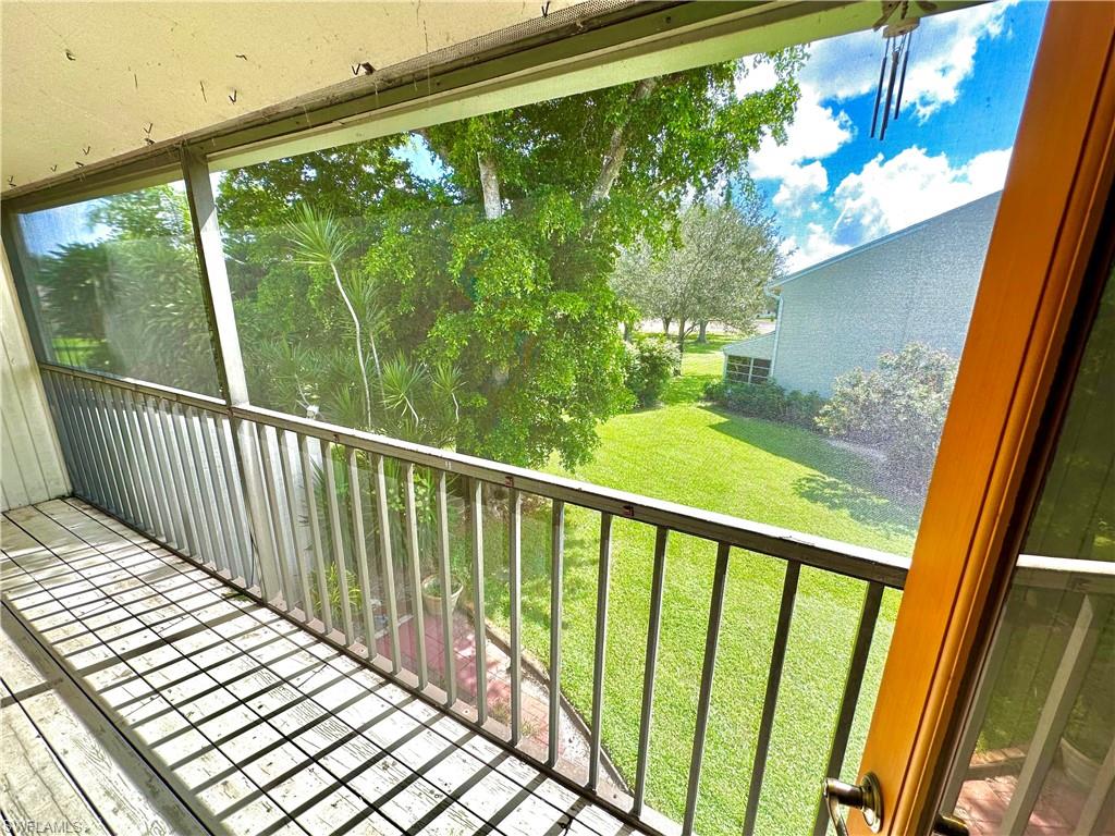 Screened balcony with wood-finish flooring, metal railing, and direct sightlines to green spaces and mature trees
