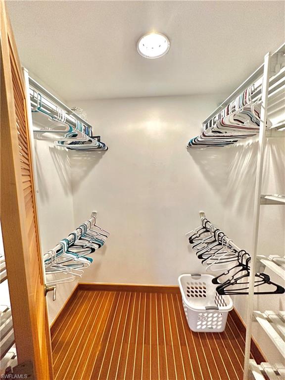 Walk-in closet featuring wood-finish flooring, white walls, recessed ceiling light, and multiple clothing rods for storage