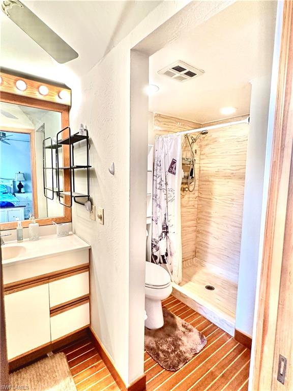 Bathroom featuring a vanity with integrated sink, wood-finish flooring, and a shower stall with light-toned tiled walls