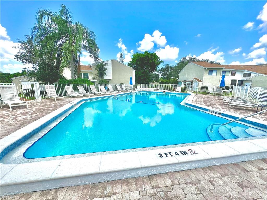 Community swimming pool featuring a tiled interior, paver deck, and perimeter fencing