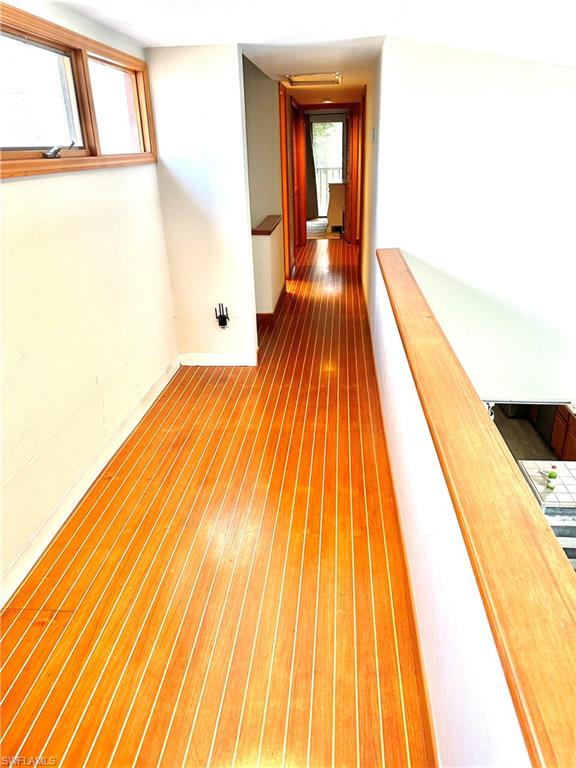 Second-level hallway featuring strip wood flooring, natural wood window trim, natural wood railings, and recessed ceiling lighting