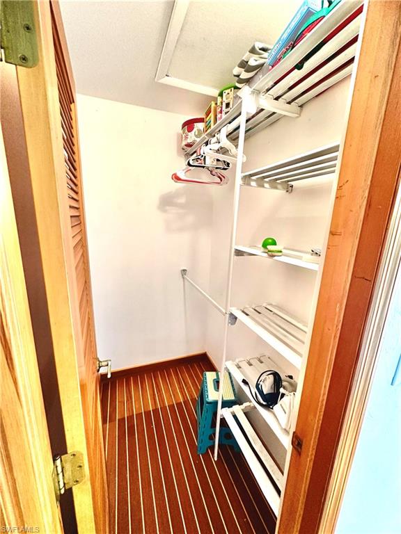 Walk-in closet with wood-finish flooring, louvered bi-fold door, white wall-mounted shelving system, and clothing rod