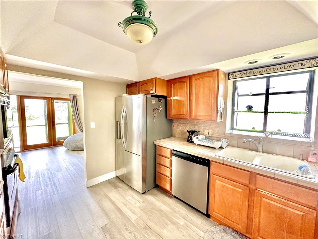 Kitchen featuring light wood-finish cabinetry, a ceramic tile countertop, and a stainless steel refrigerator