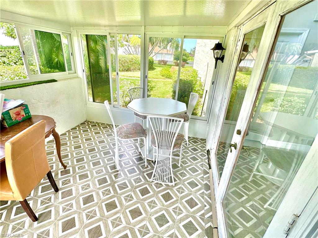 Screened-in patio featuring patterned tile flooring, multiple windows, and a glass-paneled entry door