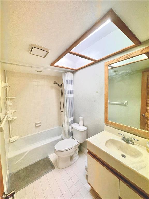 Bathroom featuring a skylight, white tiled flooring, a built-in vanity with integrated sink, and a bathtub with tiled surround