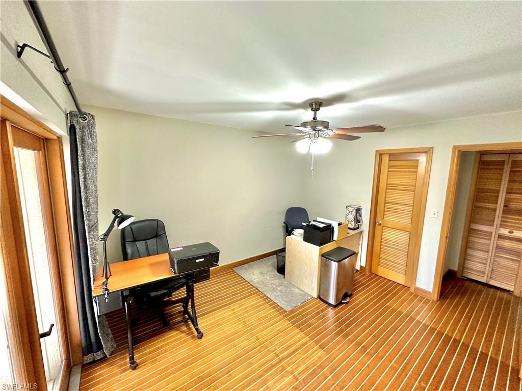 Interior room featuring wood-finish flooring, a ceiling fan with integrated lighting, and multiple louvered wooden doors
