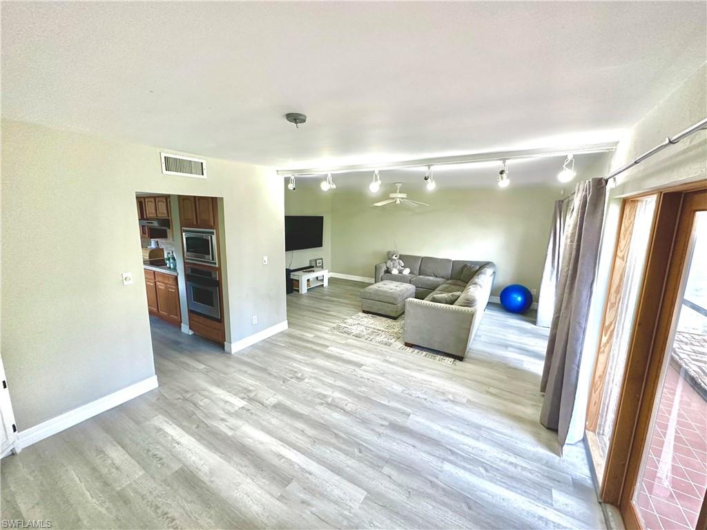 Open-concept living area with wood-finish flooring, track lighting, and a ceiling fan
