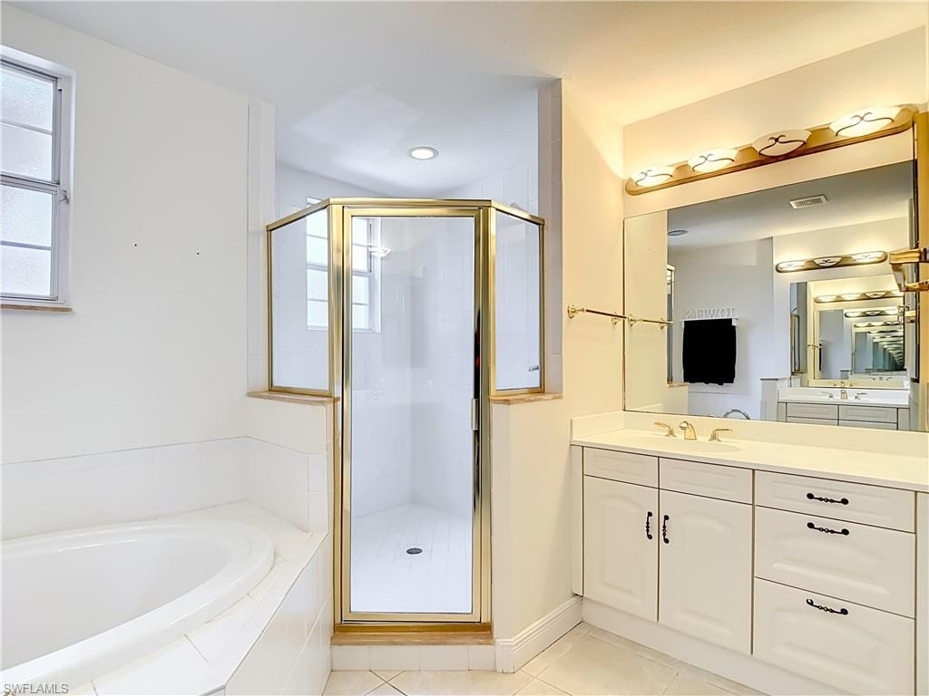Bathroom featuring a built-in soaking tub, a glass-enclosed shower with gold-tone framing, a single vanity with a large mirror, and white cabinetry