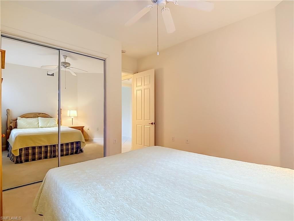 Bedroom featuring mirrored closet doors, a ceiling fan with light fixture, carpet flooring, a paneled interior door, and neutral wall tones