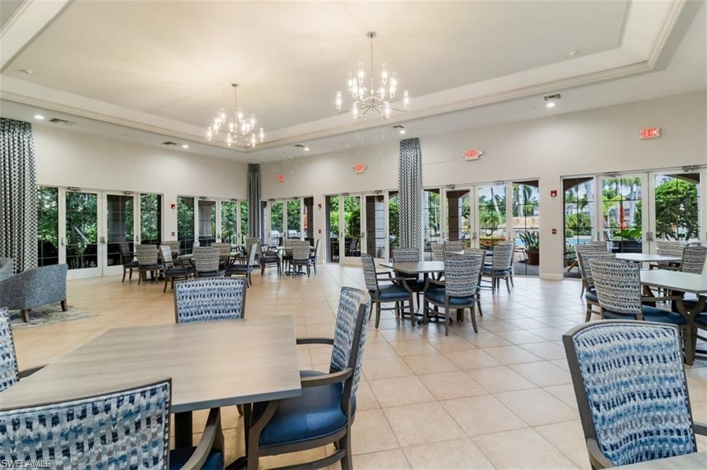 Spacious community room featuring tile flooring, multiple sets of glass French doors, decorative columns, and modern chandelier lighting
