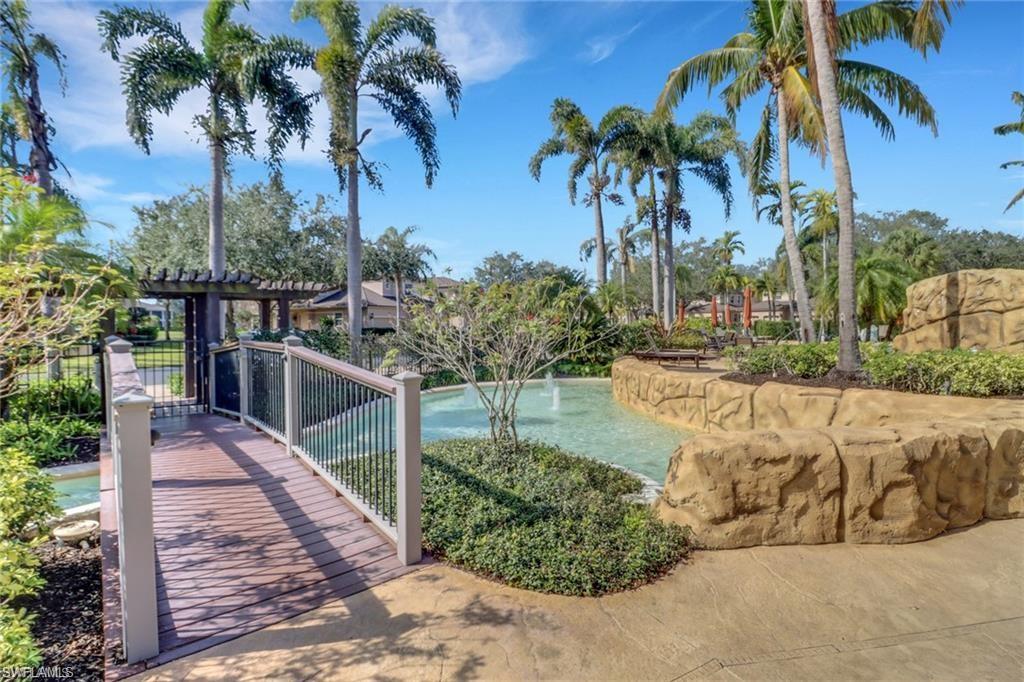 Landscaped water feature with a decorative bridge, rock-like wall, and mature palm trees