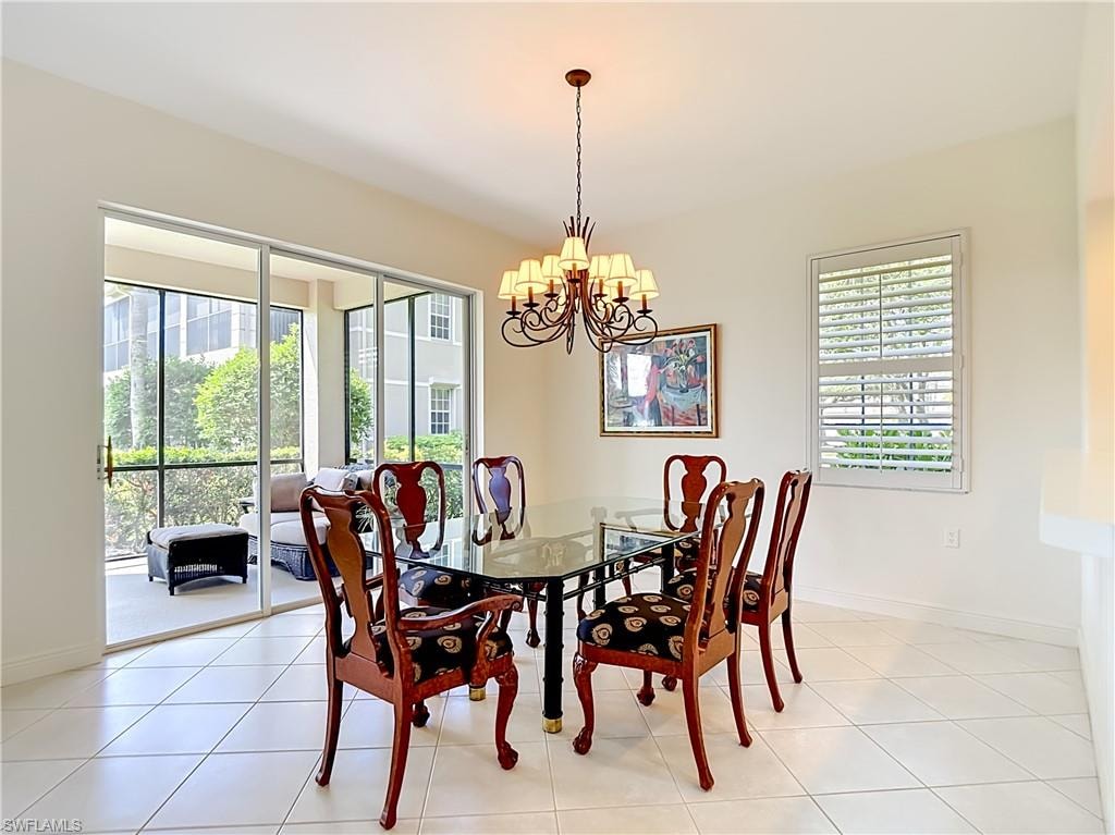 Dining area featuring a classic chandelier, sliding glass doors to a screened lanai, a window with plantation shutters, and light-toned tile flooring
