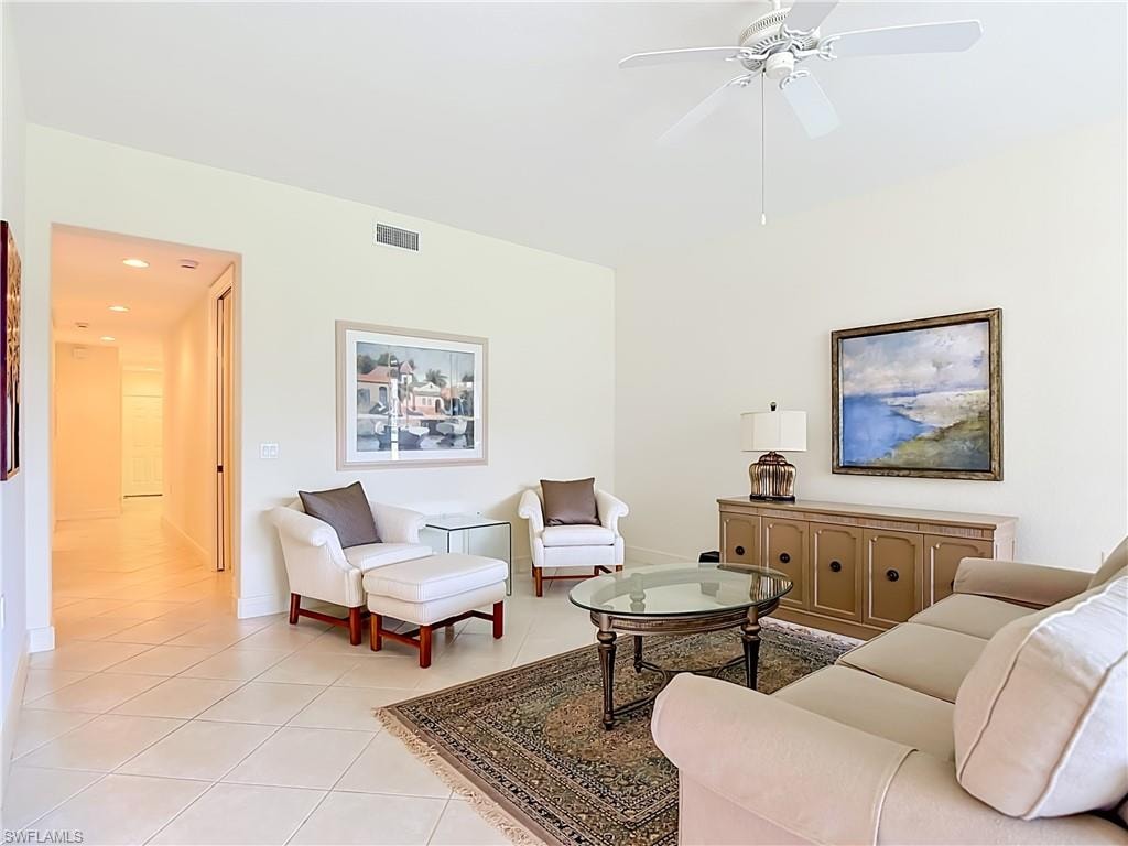 Spacious living area featuring light-toned tile flooring, vaulted ceilings, and a ceiling fan