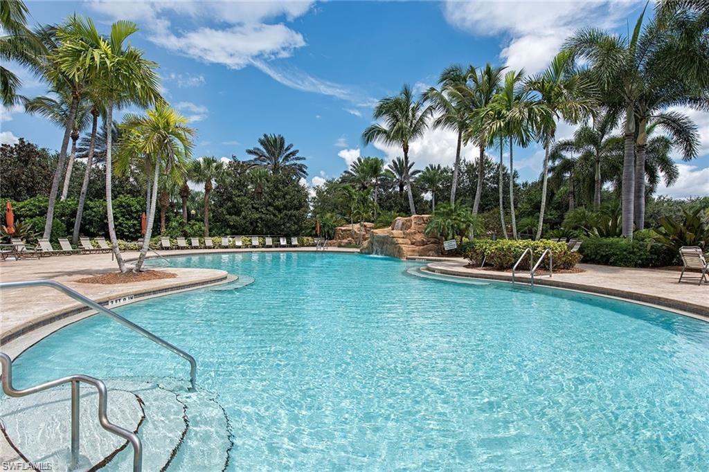 Resort-style swimming pool featuring a rock waterfall, surrounding sundeck, and lush tropical landscaping