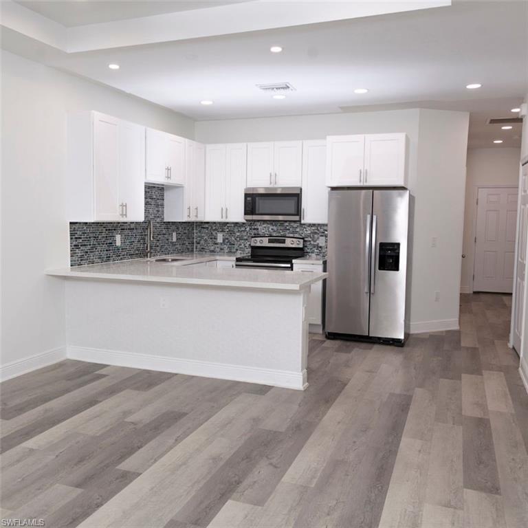 Modern kitchen featuring white shaker cabinetry, stainless steel appliances, a multi-tone tile backsplash, light-colored countertops, and wood-finish flooring