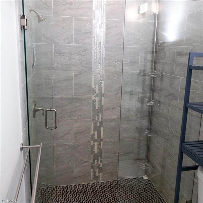 Shower enclosure featuring a glass door with a brushed nickel handle, gray rectangular wall tiles, and a vertical mosaic accent strip