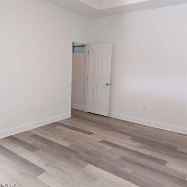 Spacious room featuring wood-finish flooring, white baseboards, and a white six-panel interior door