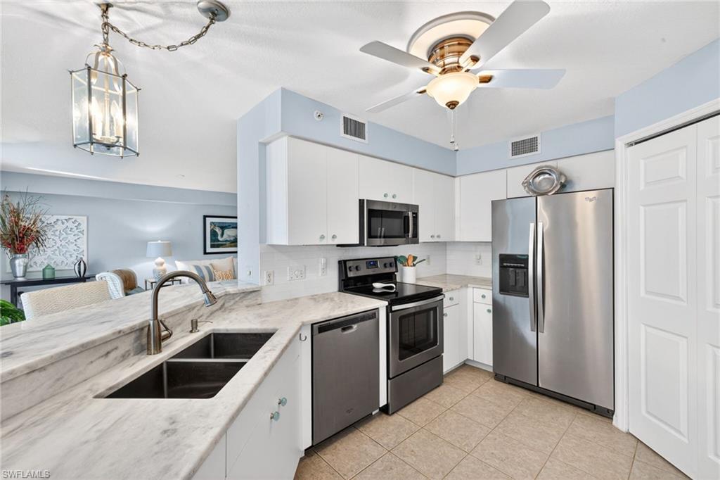 Kitchen featuring stone countertops, stainless steel appliances, white cabinetry, and tile flooring