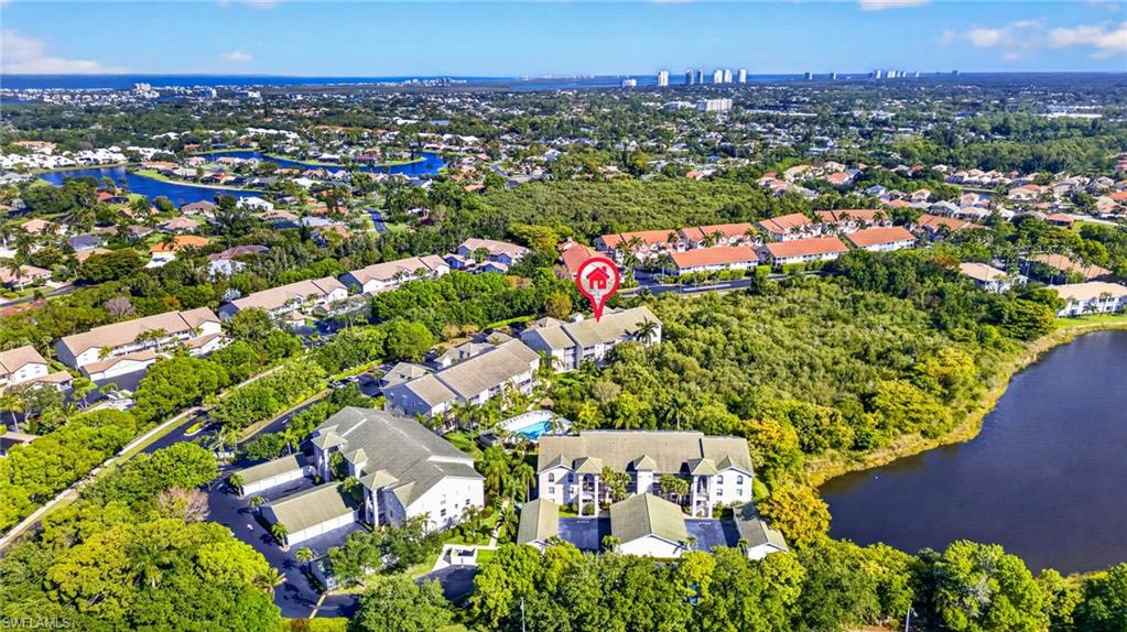 Aerial perspective featuring a community with multiple residential buildings, lush green landscaping, a prominent body of water, and distant urban skyline