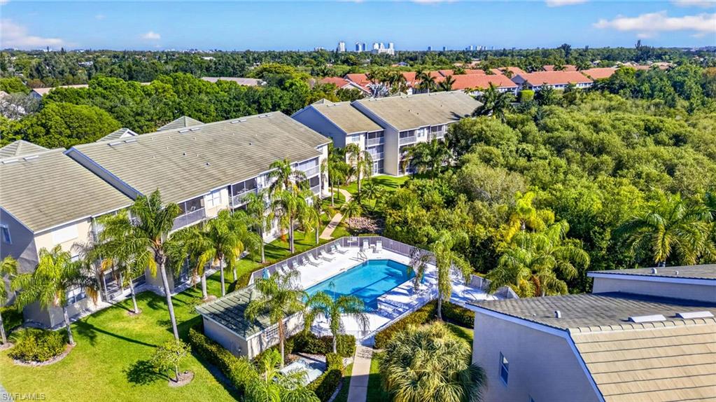 Community pool with surrounding lounge area, multiple multi-story residential buildings with balconies, mature palm trees, and manicured green spaces