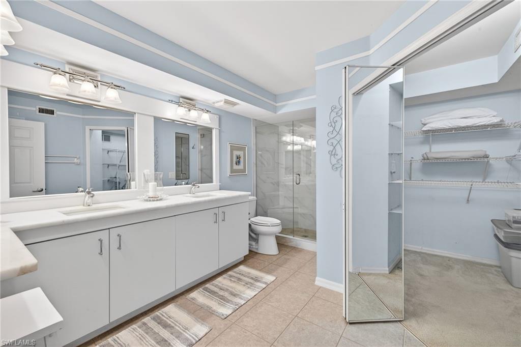 Primary Bathroom Dual vanity with white cabinetry and integrated sinks, a glass-enclosed shower with tile surround, a built-in toilet, and an expansive walk-in closet with wire shelving and a mirrored sliding door