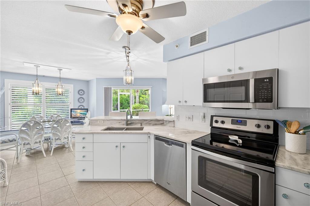 Open-concept kitchen featuring white cabinetry, stone countertops, stainless steel appliances, and tile flooring