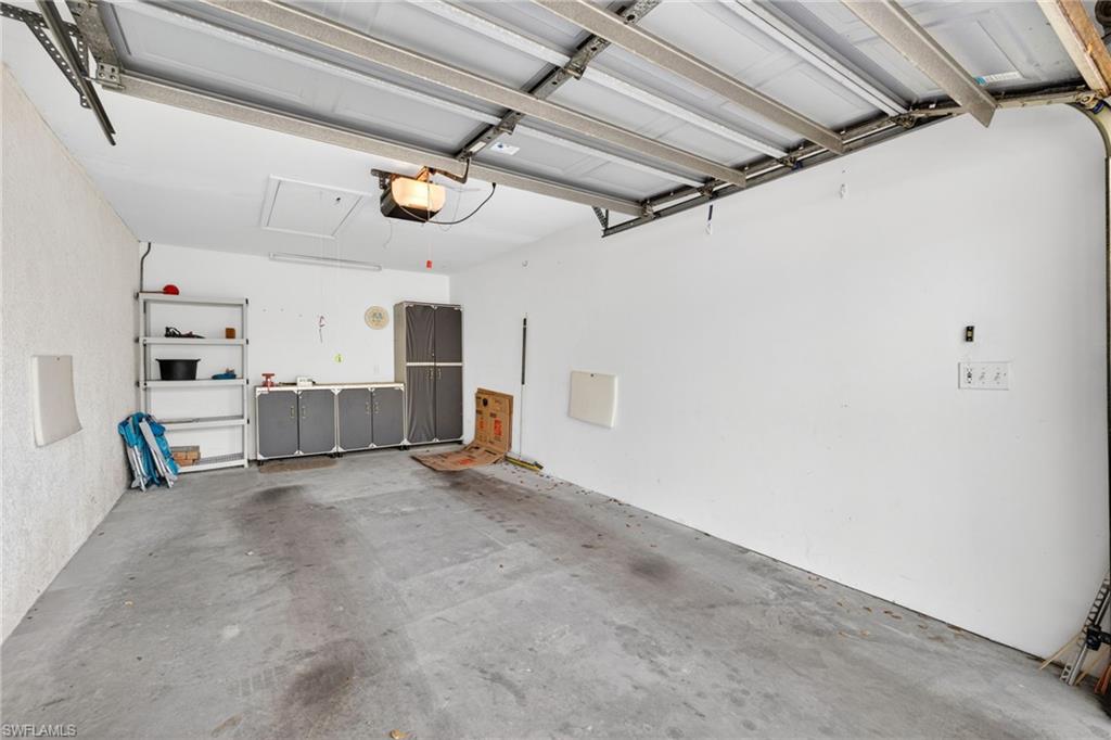 Concrete floor garage with overhead door mechanism, built-in wall shelving, integrated cabinetry, and overhead lighting