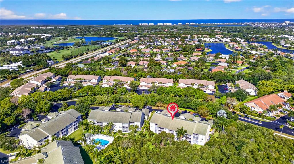 Aerial depiction of a multi-story residential building with a visible pool, surrounded by mature trees and other residential structures