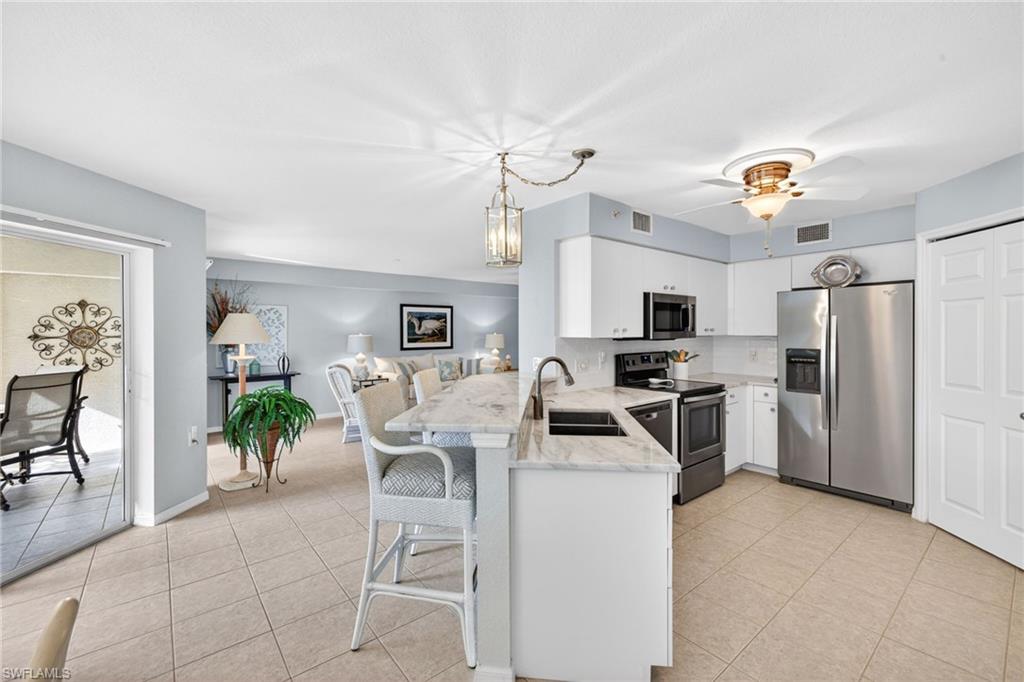 Open-concept kitchen featuring white cabinetry, stainless steel appliances, a bar-height counter, and tile flooring