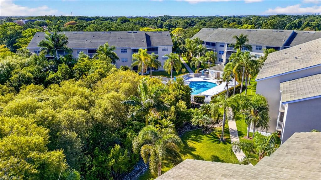 Community pool surrounded by tropical landscaping, multiple residential buildings, and walking paths