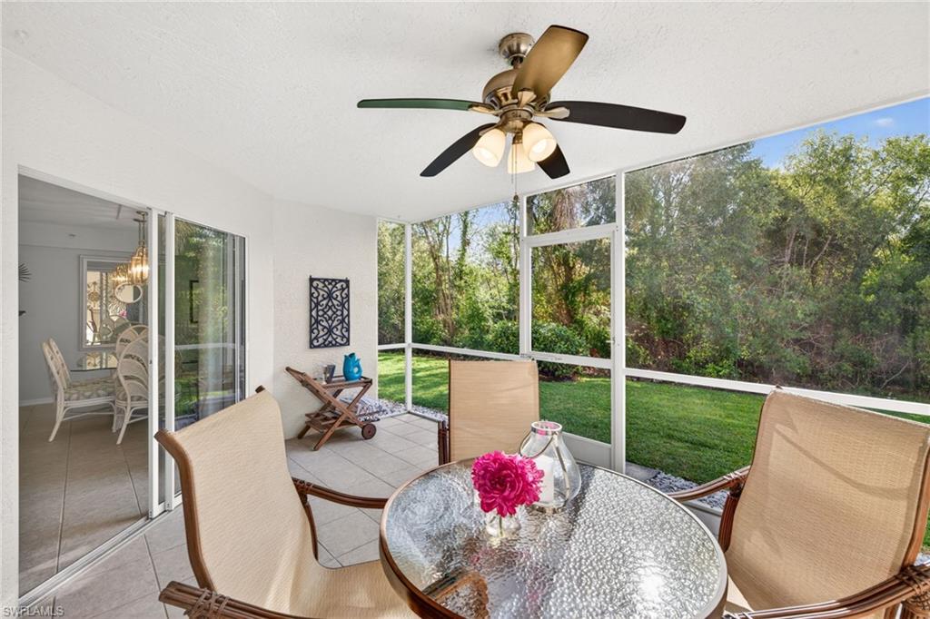 Screened lanai featuring tile flooring, a ceiling fan with integrated lighting, and a verdant backdrop